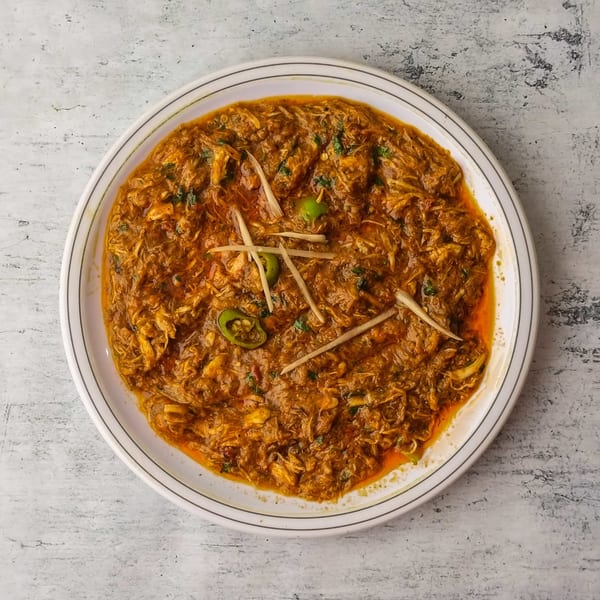 Exotic India's Indian chicken curry, garnished with ginger slivers and green chilies, on a white plate.