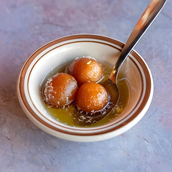 Three gulab jamun, Indian fried dough balls, in syrup with shredded coconut in a white bowl.
