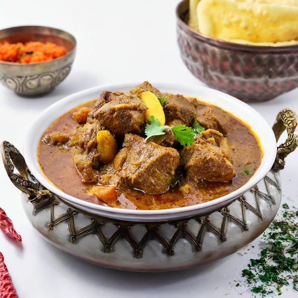 Exotic India's lamb curry with cilantro, served in an ornate bowl with naan and chutney.